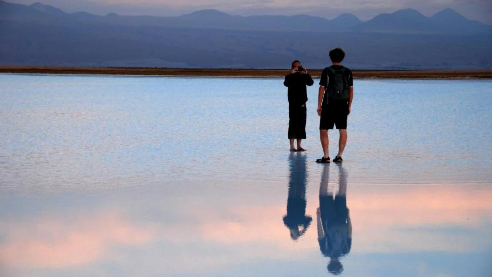 lone travelers reflected on mirror-like salt flats of Atacama under a soft horizon